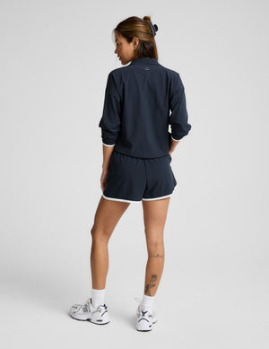 Woman wearing a blue quarter zip jacket and blue shorts with white trim against a plain background. 