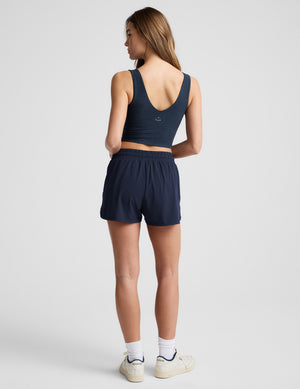 Woman wearing a blue cropped tank top and blue shorts against a plain background. 