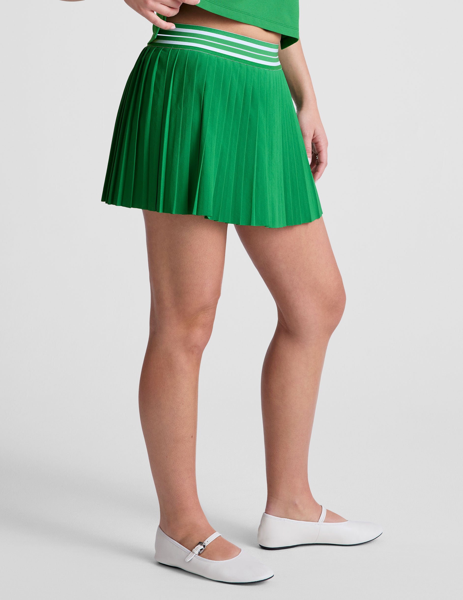 green pleated mini skirt with an exposed stripped elastic waistband​ and internal performance shorts with pockets​. 