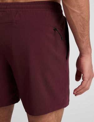 man wearing a grey t-shirt and maroon lined shorts set on a white background. 