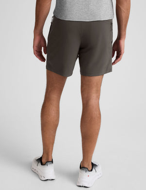 man wearing a gray short sleeve shirt and dark gray lined shorts on a plain background. 