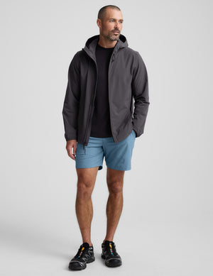 Man wearing a gray jacket and light blue shorts against a plain background. 