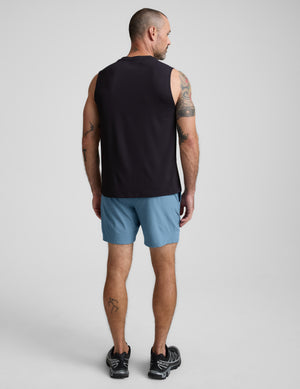 Man wearing a black sleeveless shirt and blue shorts on a plain background. 