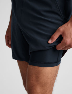 man wearing a grey t-shirt and navy blue lined shorts set on a plain background. 