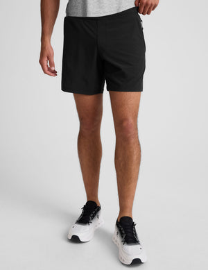 man wearing a grey crew neck t-shirt and black lined shorts on a light gray background. 