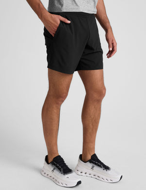 man wearing a grey crew neck t-shirt and black lined shorts on a light gray background. 