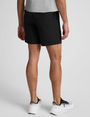 man wearing a grey crew neck t-shirt and black lined shorts on a light gray background. 