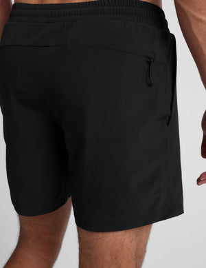 man wearing a grey crew neck t-shirt and black lined shorts on a light gray background. 