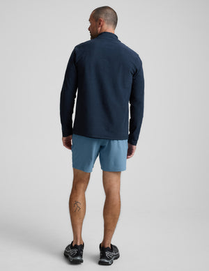 Man wearing a navy long-sleeve shirt and blue shorts on a light gray background. 