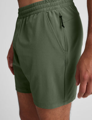 man wearing a gray t-shirt and green shorts on a white background. 
