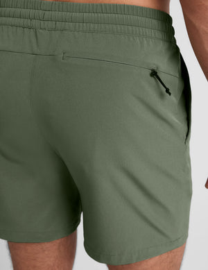 man wearing a gray t-shirt and green shorts on a white background. 