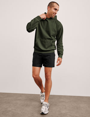man wearing a green hoodie and black shorts on a plain background. 