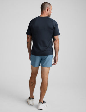 Man wearing a dark blue t-shirt and blue shorts on a light gray background. 