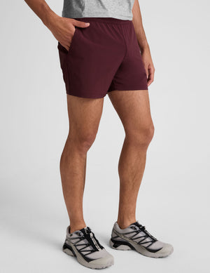 man wearing black t-shirt and maroon shorts on a plain background. 