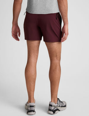 man wearing black t-shirt and maroon shorts on a plain background. 