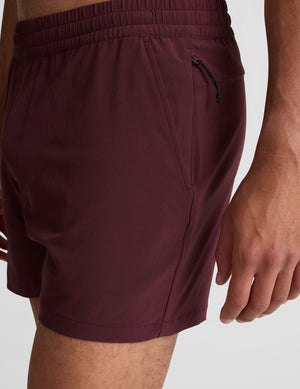 man wearing black t-shirt and maroon shorts on a plain background. 