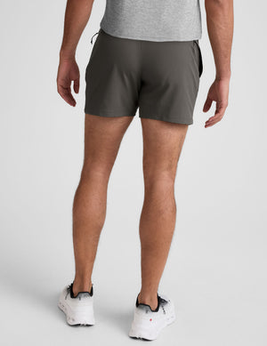 man wearing a gray t-shirt and grey shorts on a plain background. 