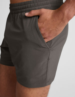 man wearing a gray t-shirt and grey shorts on a plain background. 