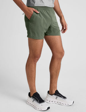 man wearing a gray t-shirt and green shorts on a plain background. 