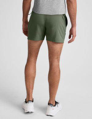 man wearing a gray t-shirt and green shorts on a plain background. 