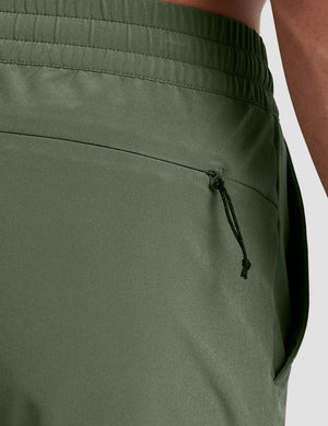 man wearing a gray t-shirt and green shorts on a plain background. 