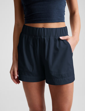 Woman wearing a navy blue tank top and shorts on a plain background. 