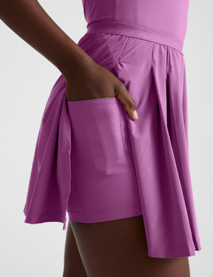 Woman wearing a purple mini dress with built-in pocket shorts against a plain background. 