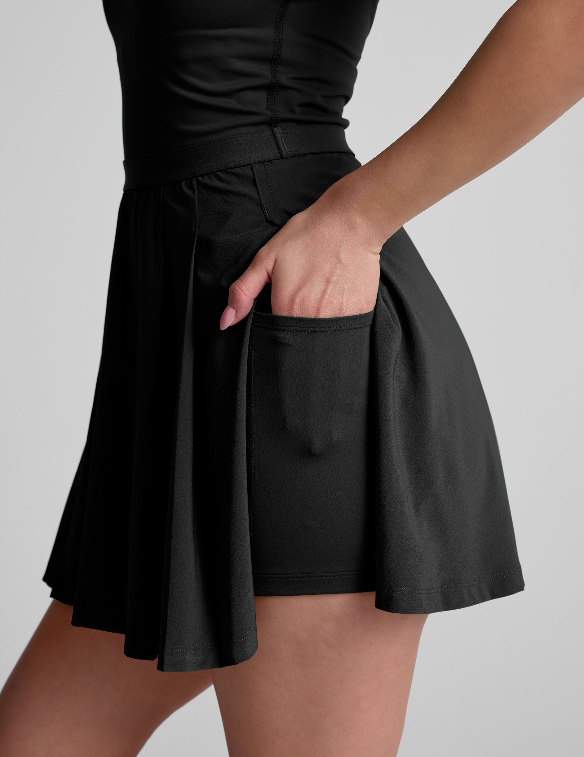 black mini dress in our stretch woven fabric with stitch down front pleats, a scoop front neckline​, open back detail​, bodice in performance stretch fabric​, and skirt side vents for easy pocket access​. 