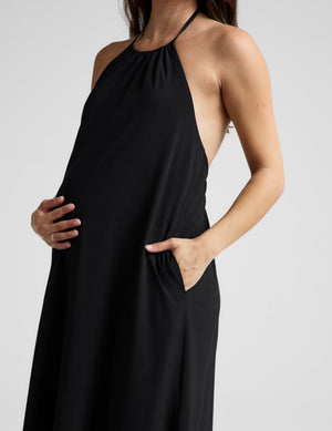 Woman wearing a black halter neck dress on a light gray background. 