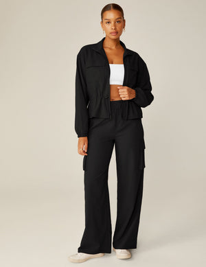 A woman wears the black City Chic Cargo Pant, featuring a wide leg, side pockets, and an elastic waist in a full-length view.