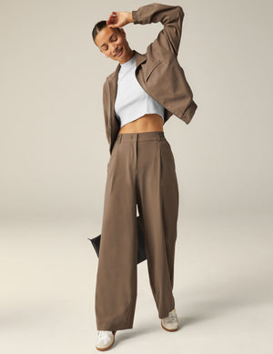 A woman wears brown Status Wide Leg Trousers with a matching jacket and white crop top, showcasing a relaxed, draped fit.