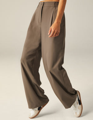 Mid-rise Status Wide Leg Trousers in Dune brown with pleats and elastic waistband, shown on a model wearing white sneakers.
