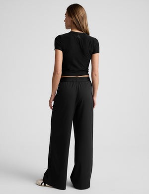 Woman wearing a black cropped t-shirt and black elasticated trouser pants against a plain background. 