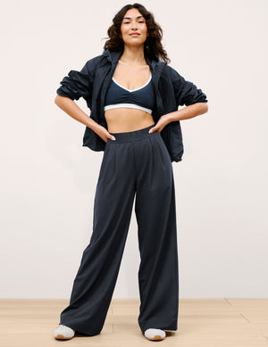 Woman wearing a navy outfit with a jacket and wide-leg pants on a plain background. 