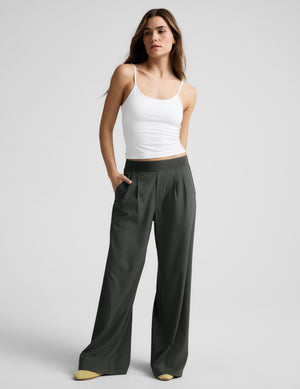 Woman wearing a white tank top and green elasticated trousers against a plain background. 