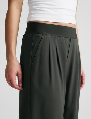 Woman wearing a white tank top and green elasticated trousers against a plain background. 