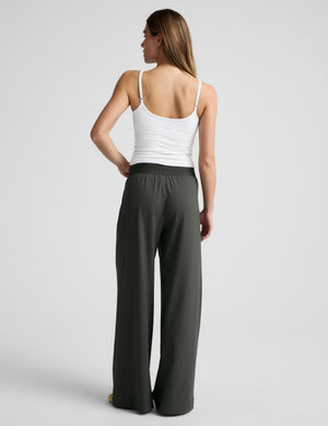 Woman wearing a white tank top and green elasticated trousers against a plain background. 