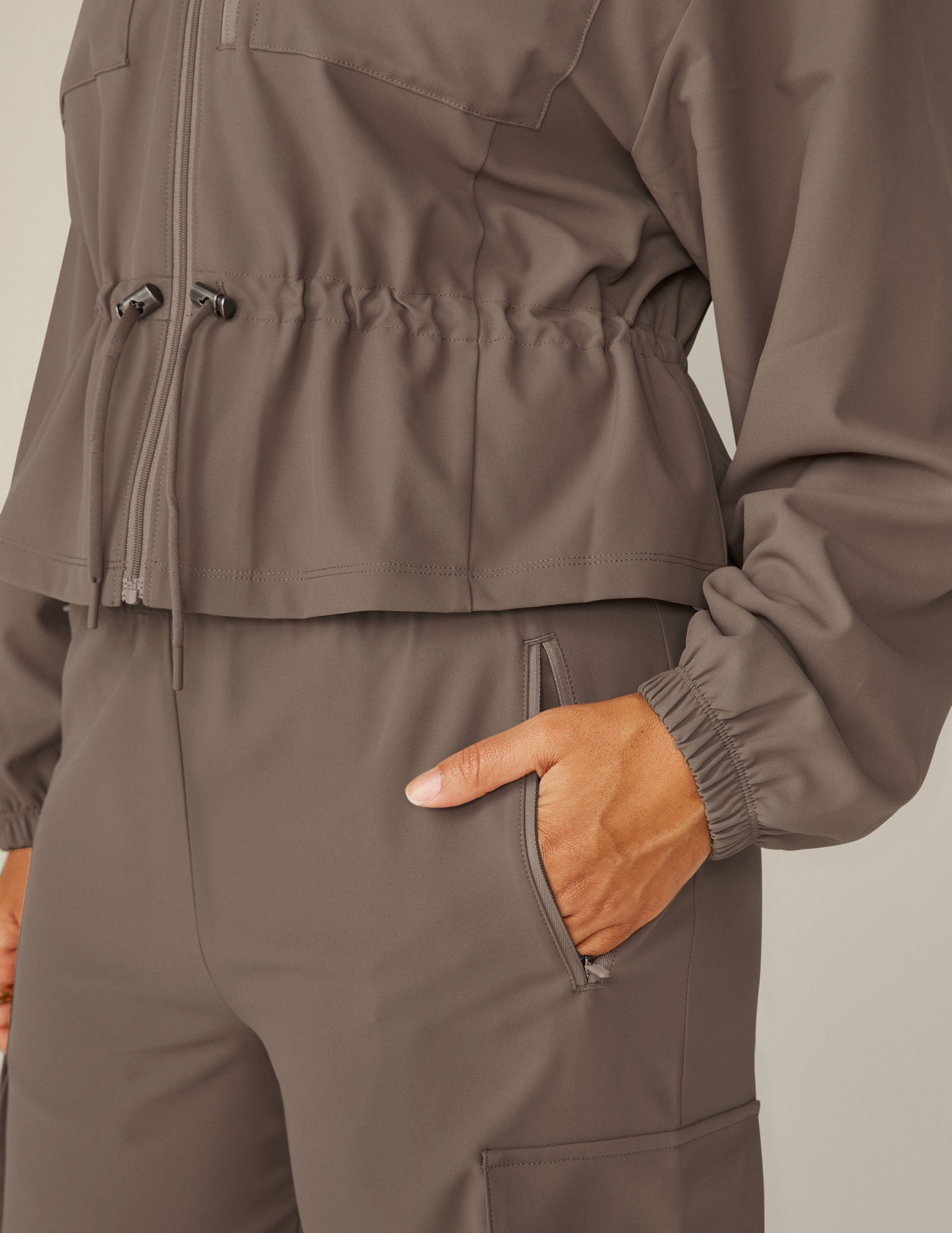 brown cargo style zip-up jacket with a drawstring tie at waist and pockets. 