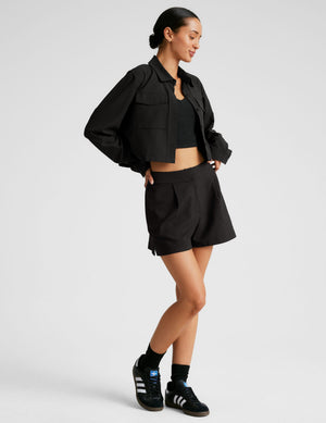 Black Midtown Trouser Short on a model, featuring a high-waisted pleated front and relaxed A-line fit with side slits.