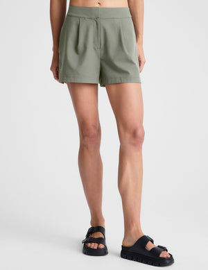 Olive green Status Shorts on a model, featuring a mid-rise waist, front pleats, and a regular fit hitting mid-thigh.