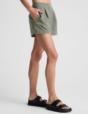 Side profile of olive green Status Shorts with front pleats and side seam pockets, featuring a tailored mid-rise fit.