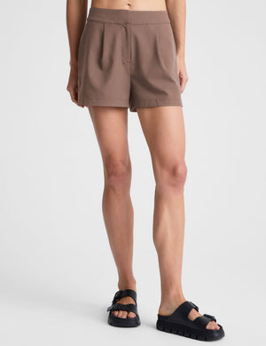 Mid-rise brown Status Shorts featuring front pleats and a straight silhouette, shown on a model with black sandals.