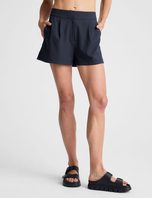 Model wears navy Status Shorts with a mid-rise fit, front pleats, and side pockets. Paired with black slide sandals.