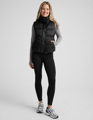 woman wearing a black puffer vest on a plain background. 