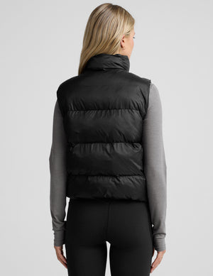 woman wearing a black puffer vest on a plain background. 