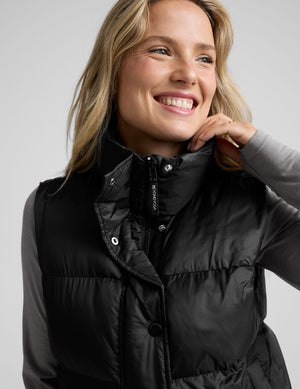 woman wearing a black puffer vest on a plain background. 