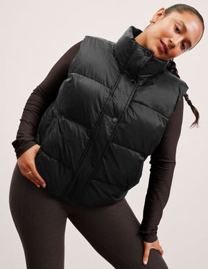 woman wearing a black puffer vest on a plain background. 