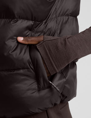 person wearing a brown puffer vest and brown long sleeve top against a plain background. 