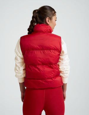 woman wearing a red puffer vest and leggings against a plain background. 