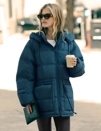 model is wearing a blue zip-up puffer jacket with a hood. 